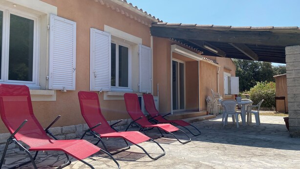 A building with a tiled patio, red lounge chairs, and a table with chairs. - Villa Avec Terrasse et Jardin (st mitre les remparts)