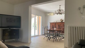 A living room with a TV, a sofa, and a dining area with a chandelier. - Villa Avec Terrasse et Jardin (st mitre les remparts)