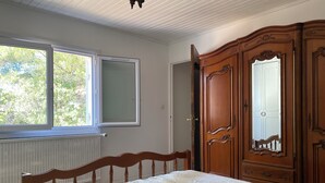A bedroom with a bed, a wooden wardrobe, a window, and a radiator. - Villa Avec Terrasse et Jardin (st mitre les remparts)