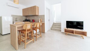 A modern kitchen with wooden cabinets, a dining area with two chairs, a built-in TV, and a staircase leading to another level.