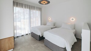 A modern hotel room with two beds, a large window with sheer curtains, a ceiling light fixture, and a wall-mounted light.
