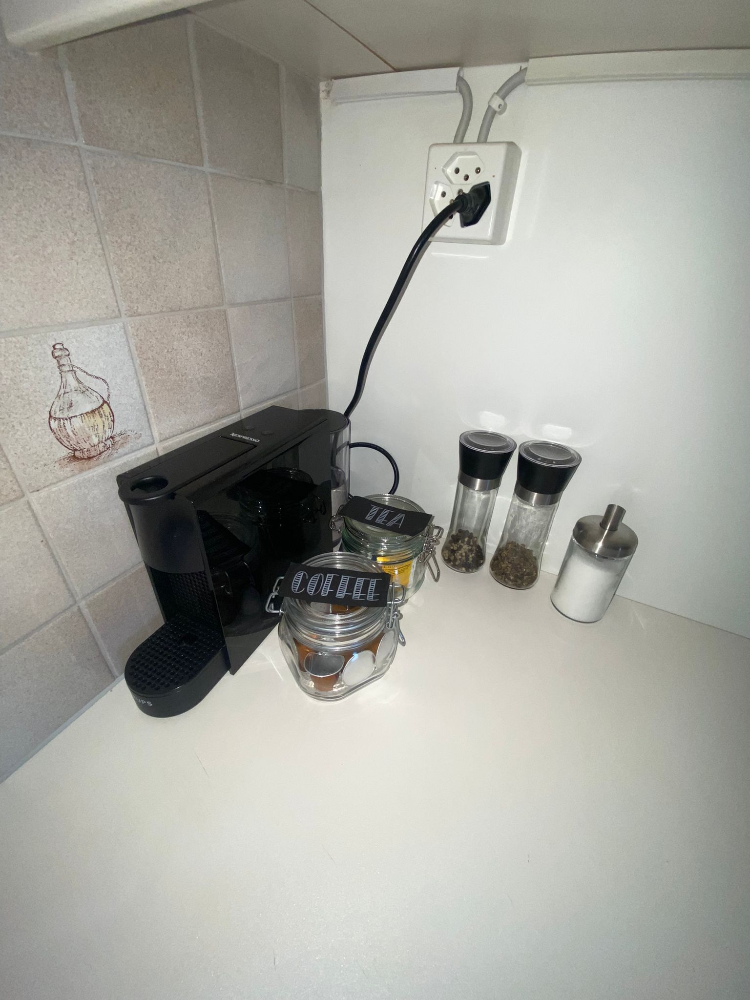 Une machine à café, deux bocaux en verre étiquetés « CAFÉ », un moulin et un récipient à épices sont posés sur un plan de travail de cuisine.