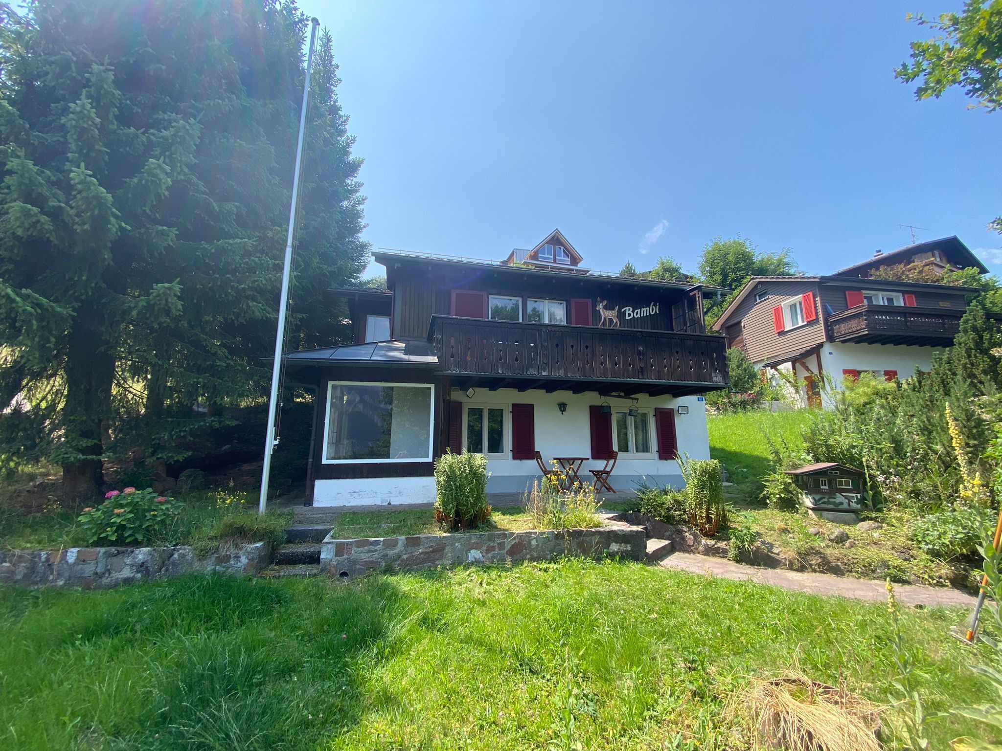 Un chalet traditionnel doté d’un balcon, d’une grande fenêtre et d’un mur en pierre à l’avant.