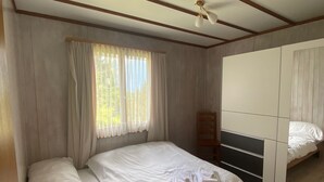 A bedroom with a wooden bed, a mirror, a ceiling fan, and a window with curtains. - Cozy 2BR Apartment with Mountainview* Free Parking (Flums)