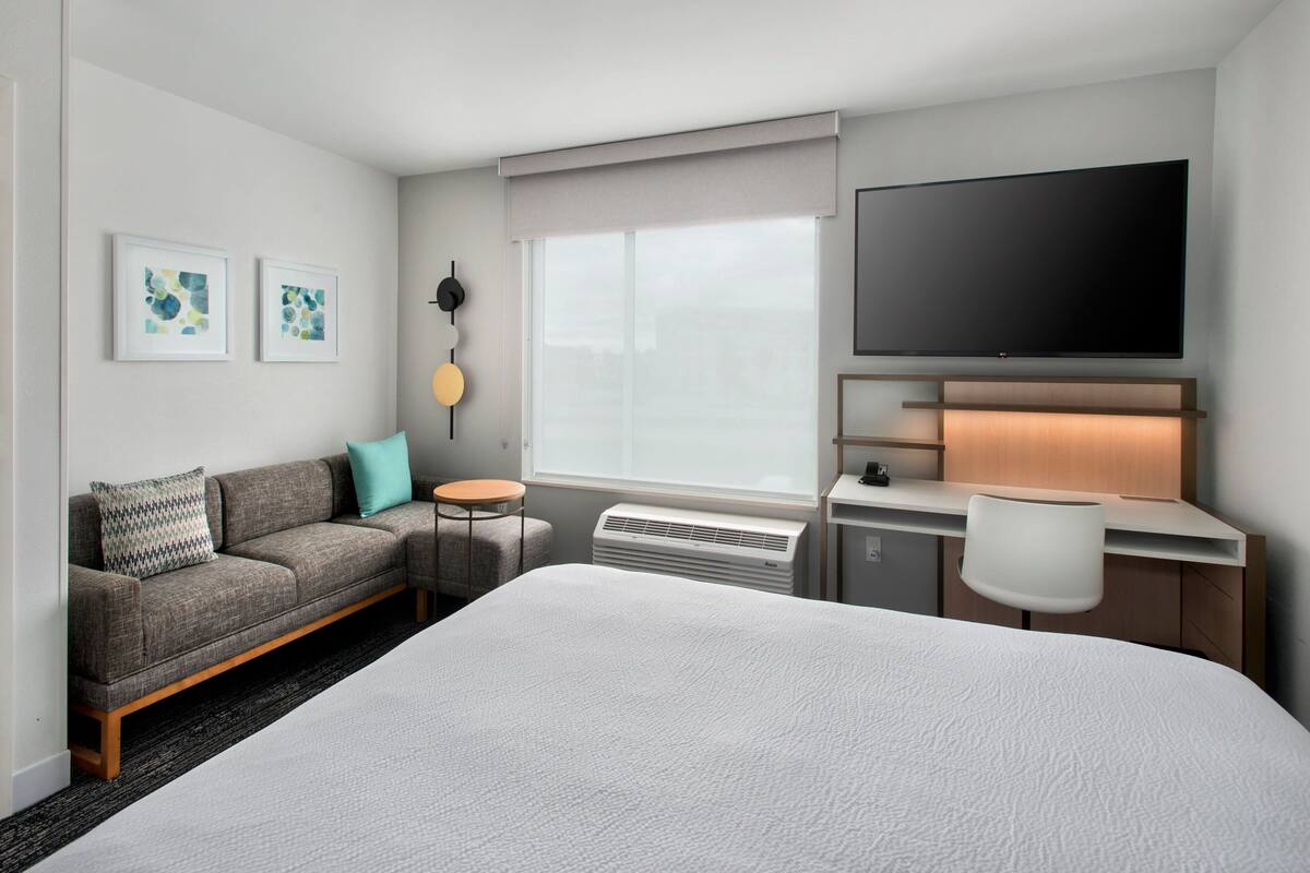 Habitación de hotel con una cama grande, un sofá, un escritorio con una silla, un televisor de pantalla plana y obras de arte en la pared.