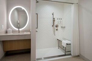 Un baño moderno con un espejo redondo, un lavamanos, una ducha con puerta de cristal y un perchero para toallas.