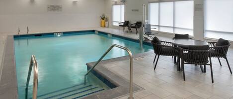 Indendørs swimmingpool med et livredder-skilt, en badestige og et opholdsområde med stole og et bord.