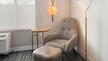 Ein modernes Zimmer mit einem gepolsterten Sessel, einem kleinen runden Tisch und einer Stehlampe.