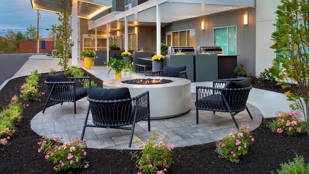 Un espace extérieur moderne, aménagé avec des sièges, comprenant un foyer circulaire, entouré de chaises en osier noir et un patio couvert.