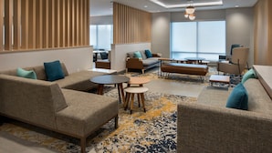 Un hall d’hôtel moderne, doté de canapés, de tables et d’une grande fenêtre.