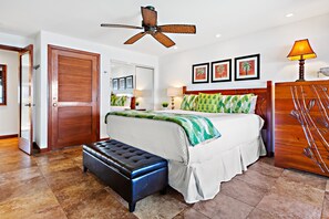 A bedroom with a bed, a bench, a ceiling fan, and a wooden wardrobe. - Chic 1bd condo, granite kitchen and Pacific views (Lahaina)