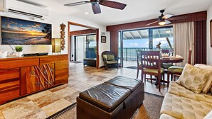 Un vaste espace de vie comprenant un grand téléviseur à écran plat, un ventilateur de plafond, une table à manger avec des chaises et un balcon avec vue.