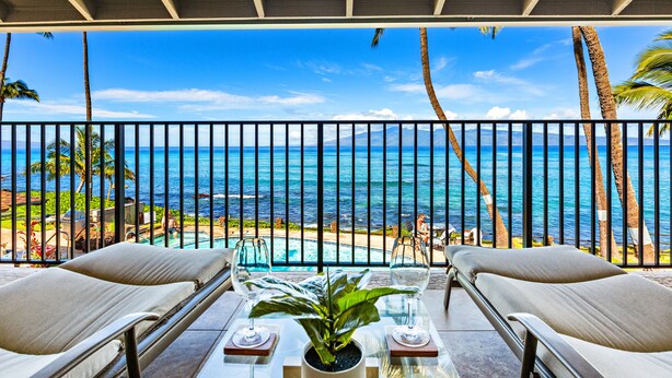Un balcon avec vue sur l’océan, deux fauteuils de relaxation, une table avec une plante et une rambarde en verre.