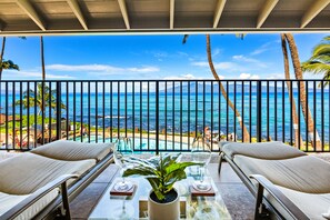Ein Balkon mit Meerblick, zwei Liegestühle, ein Tisch mit Pflanze und ein Glasgeländer.