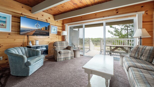 A cozy cabin interior with a plaid sofa, armchair, and a flat-screen TV mounted on the wall. - Great oceanfront townhome on 67th Street with multiple decks to enjoy the Atlantic Ocean (Ocean City)