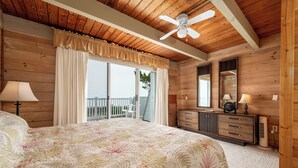 A bedroom with a large bed, wooden walls, a ceiling fan, a dresser, and a window with a view of a balcony. - Great oceanfront townhome on 67th Street with multiple decks to enjoy the Atlantic Ocean (Ocean City)