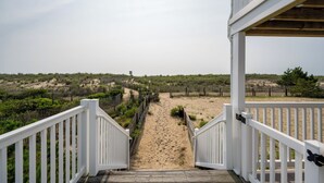 A wooden deck leading to a sandy beach area with white railings and a view of the beach and dunes. - Great oceanfront townhome on 67th Street with multiple decks to enjoy the Atlantic Ocean (Ocean City)