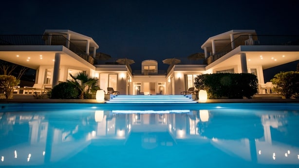 Un hotel moderno con una piscina grande, varios balcones y una entrada bien iluminada.