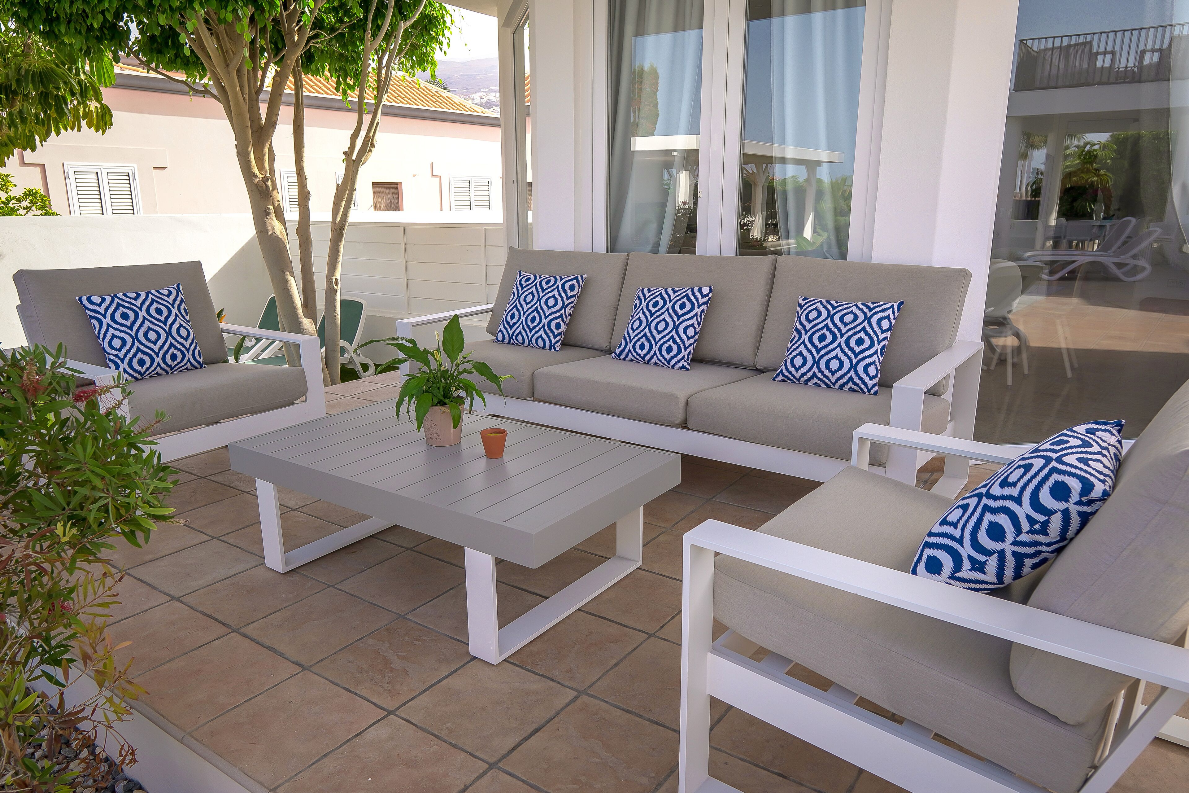 Un espace extérieur moderne aménagé avec un canapé et des fauteuils, une table basse et une plante en pot.