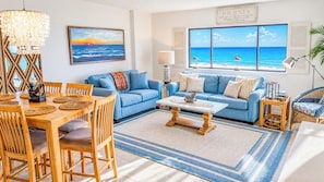 A living room with a dining area, a large window with a view of the ocean, and a chandelier. - Shalimar 2B! Oceanfront Bliss! 2BR Condo with Balcony Access from BOTH Bedrooms! (North Myrtle Beach)