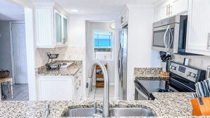 Cocina con gabinetes blancos, encimeras de granito, electrodomésticos de acero inoxidable y vistas al exterior.