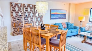 A dining area with a wooden table and chairs, a decorative wall panel, and a hanging light fixture. - Shalimar 2B (North Myrtle Beach)