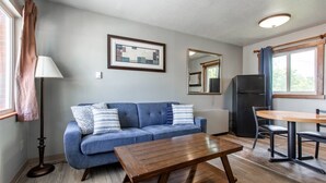 Ein Zimmer mit einem blauen Sofa, einem Holztisch, einem Spiegel, einem gerahmten Bild und einem schwarzen Kühlschrank.