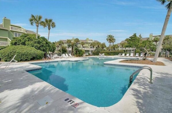 A swimming pool with lounge chairs, surrounded by palm trees and buildings.