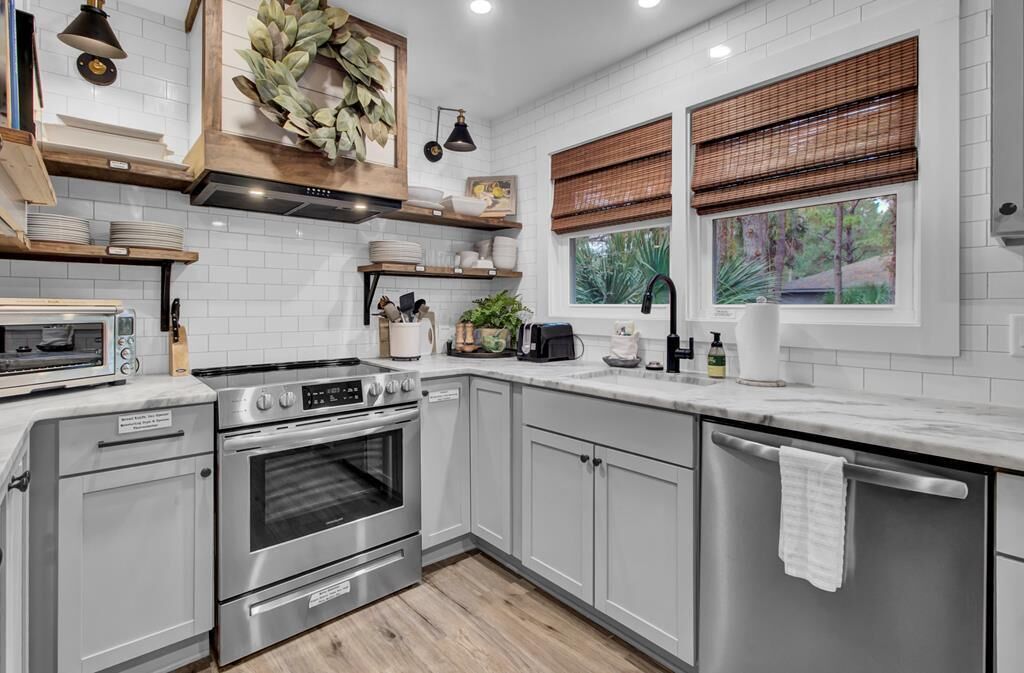 A modern kitchen with white cabinetry, stainless steel appliances, and a window with a view of greenery.