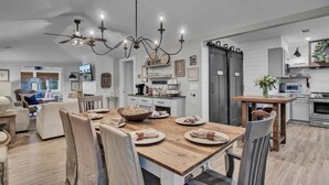 A spacious kitchen with a wooden dining table, modern appliances, and a chandelier. - Little Cottage by the Sea | Hot Tub & Walk to Beach (Isle of Palms)