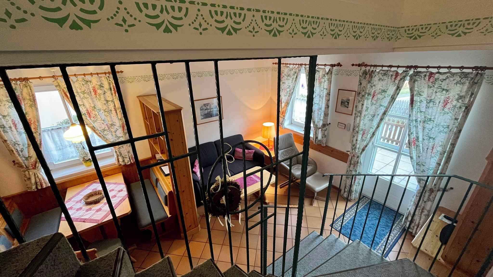 Ein gemütliches Wohnzimmer mit einer Couch, Sesseln, einem Tisch und einer Treppe, die zu einer weiteren Ebene führt.