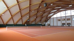 An indoor tennis court with a high, arched wooden ceiling and a green floor.