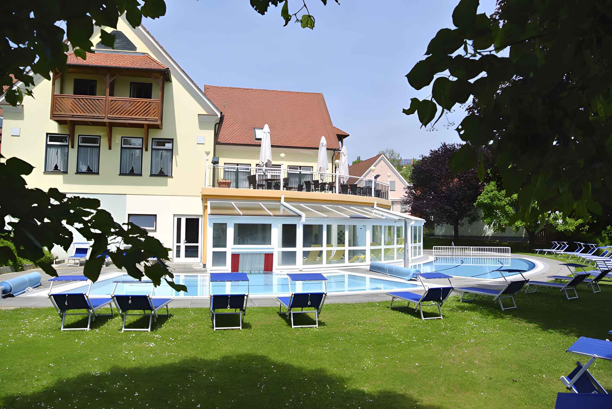 A hotel with a swimming pool, sun loungers, and a covered outdoor area.