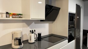 Una cuina moderna amb armaris blancs, un microones integrat i una cafetera a la tauleta.