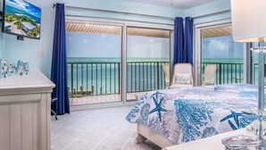 A bedroom with a bed, a ceiling fan, a TV, and a view of the ocean.