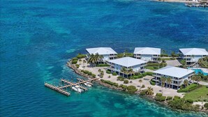 A coastal property with multiple buildings, a dock with boats, and clear blue waters.