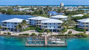 A coastal property with multiple two-story buildings, a dock with boats, and a clear view of the ocean.