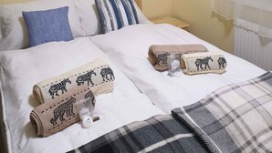 A double bed with white bedding, two pillows, a blue pillow, and a striped pillow. There are two rolled towels with animal prints on the bed.