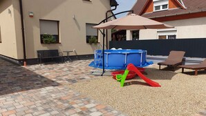 A backyard with a blue pool, a red slide, and a beige house with a brown roof.