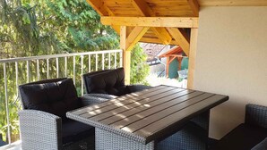 An outdoor patio with wicker furniture, a wooden table, and a white railing.