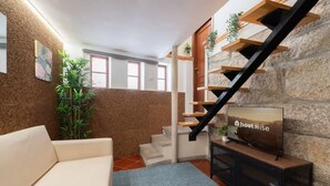 En moderne stue med sofa, fjernsyn, trappe med træhylder og en plante.