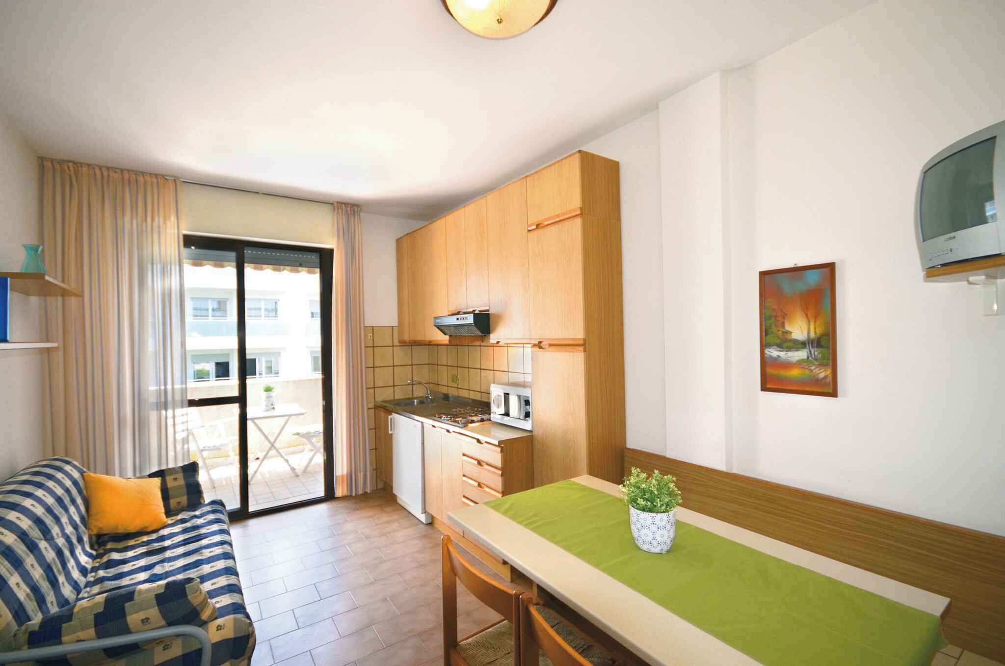 Un espacio habitable compacto con kitchenette, zona de comedor y sofá con cojines.