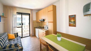 Un espacio habitable compacto con kitchenette, zona de comedor y sofá con cojines.