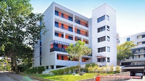 A modern multi-story building with balconies, a gated parking area, and a landscaped garden.