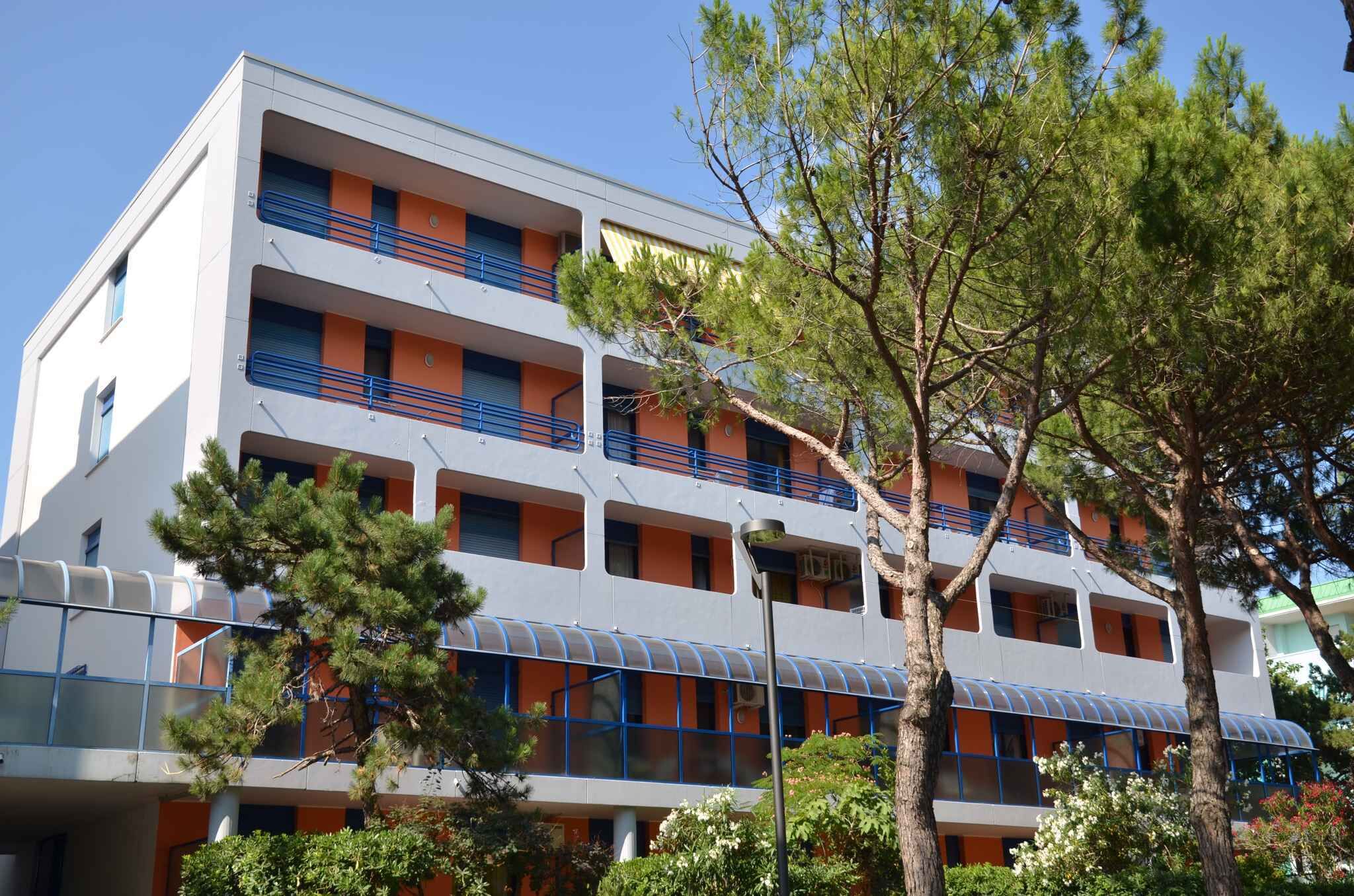 Ein mehrgeschossiges Hotel mit Balkonen, einem überdachten Gang und umgebender Bepflanzung.