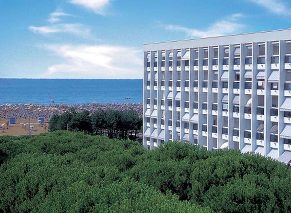A modern hotel with a grid-like facade, located near a beach with visible umbrellas and people.