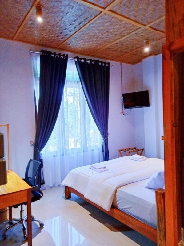 A bedroom with a bed, a desk, a chair, a TV, and a window with curtains.