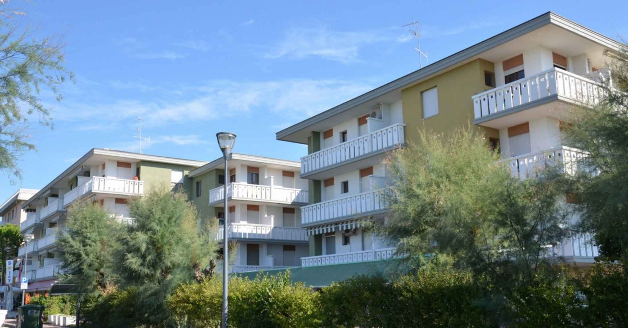 Un immeuble résidentiel à plusieurs étages, doté de balcons, d’un lampadaire et entouré de verdure.