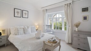 Quarto com uma cama grande, uma mesa de cabeceira, cômoda, uma cadeira e uma janela com cortinas.
