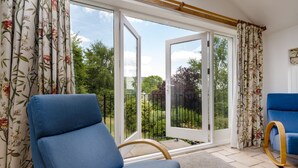 Una habitación con una silla azul, un sofá azul y vistas de un jardín a través de un ventanal.